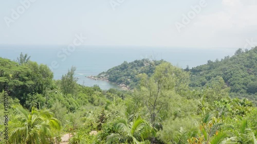 Scenic midday view from a tropical hilltop on Praslin Island, Seychelles, overlooking the Indian Ocean, marina, and green foliage under a blazing sun and blue sky