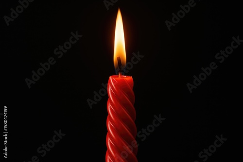 Elegant twisted red candle burning brightly against a dark background with a large flame