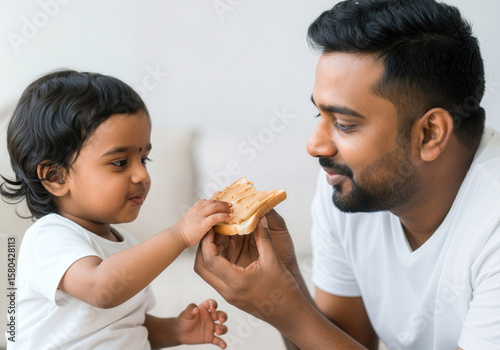 Indian father bonding with toddler daughter while sharing a slice of peanut butter toast at home, warm and nurturing moment
