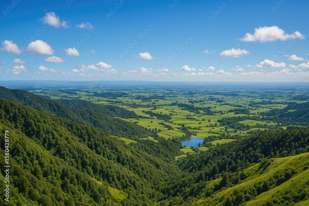 Fototapeta premium A breathtaking landscape viewed from a mountain summit, showcasing expansive rolling hills, vibrant greenery, and farmland under a clear blue sky