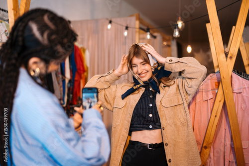 Fashionable Young Woman Posing in Clothing Shop with Friend Taking Photo