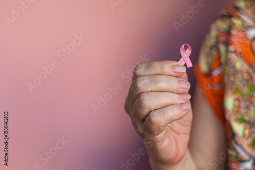 Fotografía Close-up image of an elderly woman wearing an orange robe with decorative ornaments, gently holding a pink breast cancer awareness ribbon