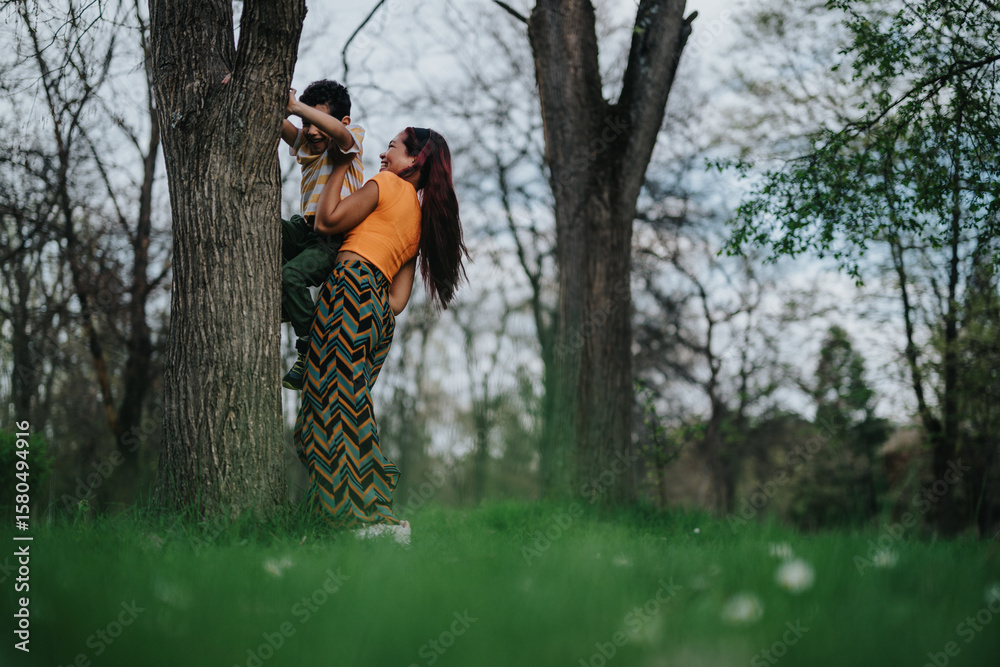 A Filipino mother and her child share a moment in nature as she supports his climb up a sturdy tree against a serene, lush green park background. A Filipino mother and her child share a moment in nature as she supports his climb up a sturdy tree against a serene, lush green park background.