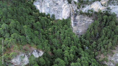 Aerial footage of a waterfall in rocky green forests high at the mountains