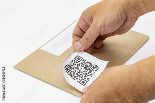 Person is attaching dummy QR code label to brown envelope, demonstrating modern and efficient way to manage information. hands are carefully placing label, indicating attention to detail