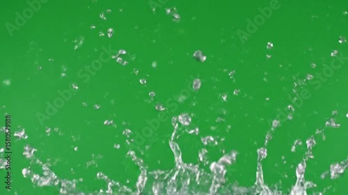Dynamic slow motion water splash explosion with crystal clear droplets spreading outward against the solid green screen background for visual effects.