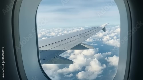 View from an airplane window showcasing a wing above fluffy clouds during daylight travel