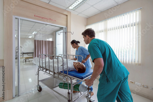 Two healthcare worker are hurriedly transferring a patient on a stretcher in a bright hospital emergency room during the day, illustrating urgency and teamwork in medical care.
