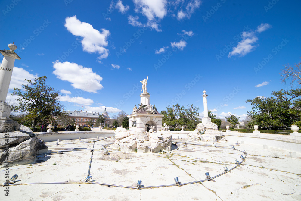 Fototapeta premium Fountain in Aranjuez, Spain surrounded by clear skies and historical architecture during a sunny afternoon