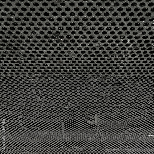 Industrial metal grate texture with numerous circular holes, showing signs of wear and dirt. A close-up view of the grate with no people or objects.