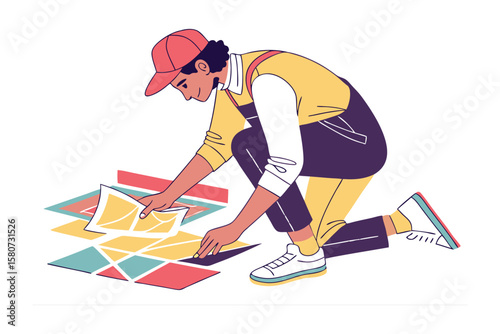A person in a red cap and yellow overalls kneels carefully arranging colorful geometric tiles on a white background showcasing a creative design process