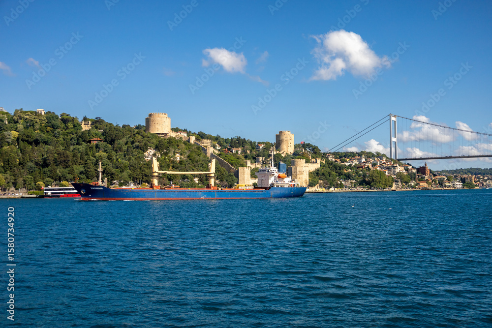 Fototapeta premium Cargo Ship Passing by Rumeli Fortress and Bosphorus Bridge in Istanbul