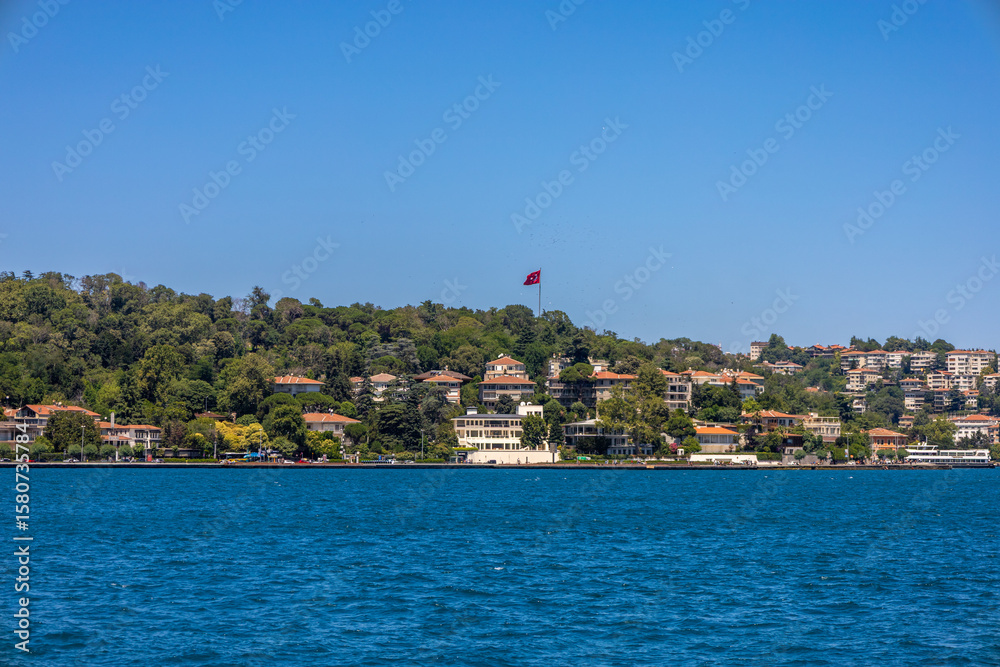Fototapeta premium Turkish Flag Above the Bosphorus Hills in a Lush Coastal Neighborhood