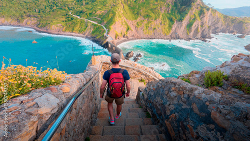 Slika na platnu A male hiker with a red backpack descends the famous stone staircase leading to the iconic San Juan de Gaztelugatxe hermitage, a stunning travel destination on the coast of Biscay