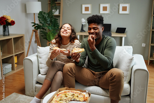 Happy couple laughing and eating pizza on sofa at home