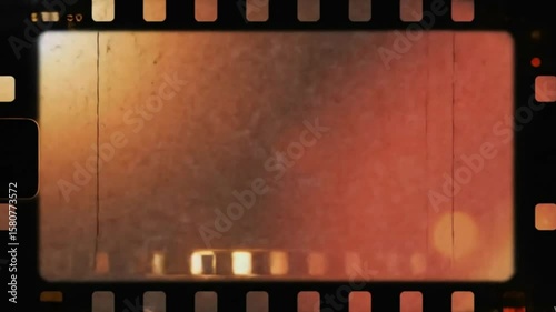 Old film strip with visible sprocket holes scratches and blurred warmtoned light spots on the frame