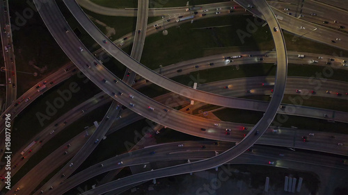 Aerial view of a sprawling highway interchange with ribbons of light tracing the paths of cars against the dark backdrop of the city, Dallas, Texas, United States.
