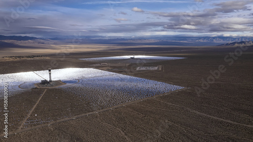 Aerial view of the stark, sun-drenched Ivanpah Solar Electric Generating System shimmers against the arid desert landscape under a vast, dramatic sky, California, San Bernardino County, United States. photo