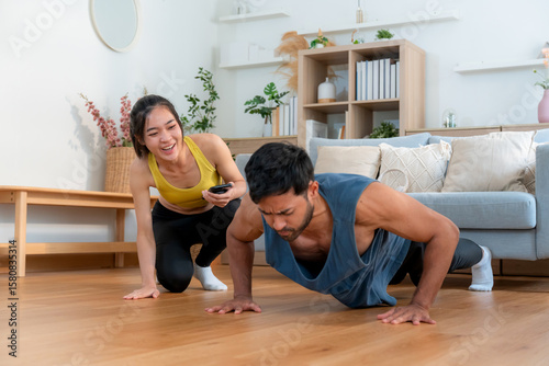 Young asian couple workout during woman hold smartphone encouragement to partner while man doing pushup with motivation, woman cheering man with exercise with strong and strength, self-care.