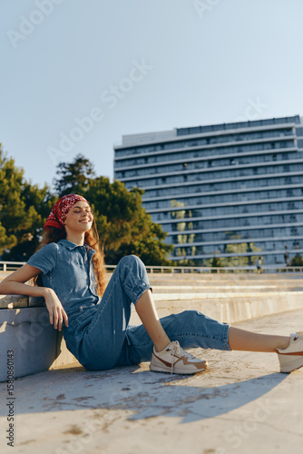 Lifestyle woman in modern boho-western denim street style relaxing outdoors under warm sunlight with a film color aesthetic and casual sneakers.