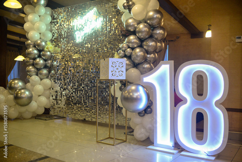Decoration as a background for photography with white and gray balloons, glitter, neon sign Happy Birthday in England and a large number eighteen that has led lighting
