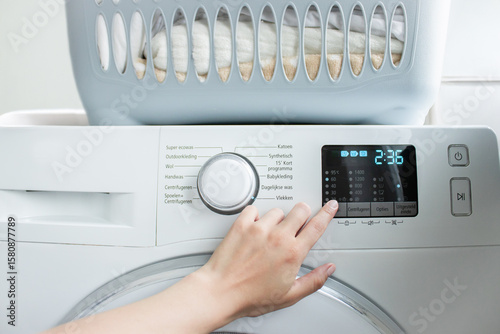 Close-up of a hand pressing a button on a washing machine with laundry inside. Concept of starting a wash cycle, dirty clothes, household chores, hygiene, and modern appliances.