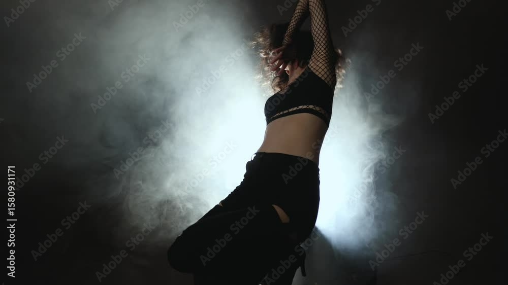Modern dance concept: young woman in chic black ensemble moving through atmospheric smoke effects