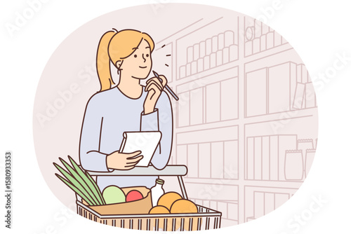 Woman walks around supermarket with cart filled with vegetables and holds checklist in hands