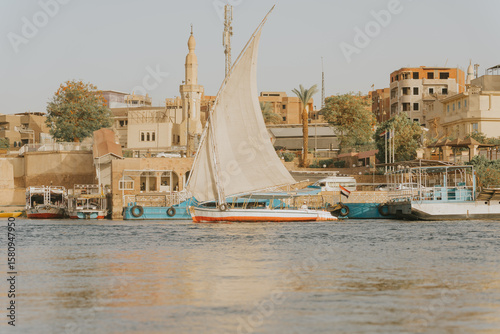 Felucca sailing on the nile river in egypt, passing traditional houses and mosques