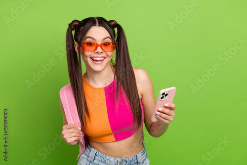 Smiling young woman with colored pigtails holding a pink smartphone against a vibrant green background