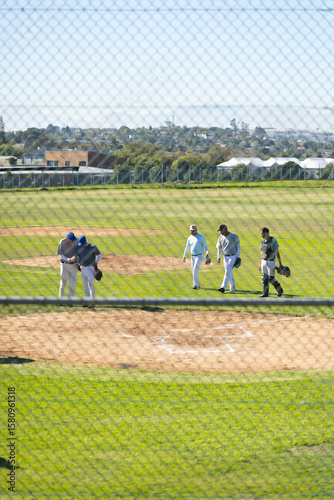 Male teammates walking and talking on baseball infield carrying gloves and wearing catcher's helmet