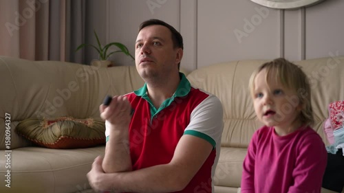 A dad and daughter bond while watching TV at home, using the remote control. The dad channel surfs for entertainment