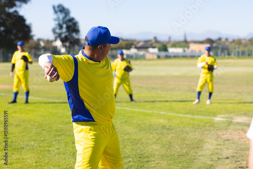 Group of men holding baseball gloves and wearing blue caps pitching and fielding on baseball field