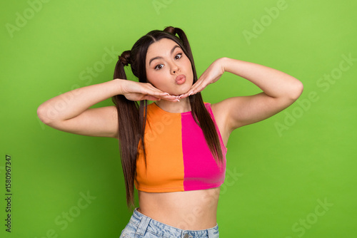 Trendy young woman with ponytails posing playfully in bright summer casual attire against a green studio background