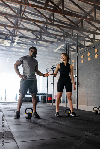 Diverse training partners in gymwear greeting each other in gym over kettlebells near weight plates