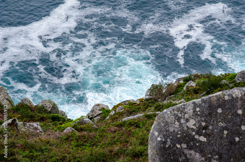 Dramatic top view of ocean waves hitting rugged rocks and green cliff, showcasing natural beauty and coastal wilderness. Ideal for travel, nature, and landscape themes.