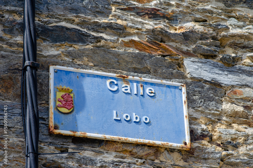 Obraz premium Vintage blue street sign Calle Lobo with a Spanish crest mounted on an old textured stone wall, capturing authentic local atmosphere in a Spanish village.