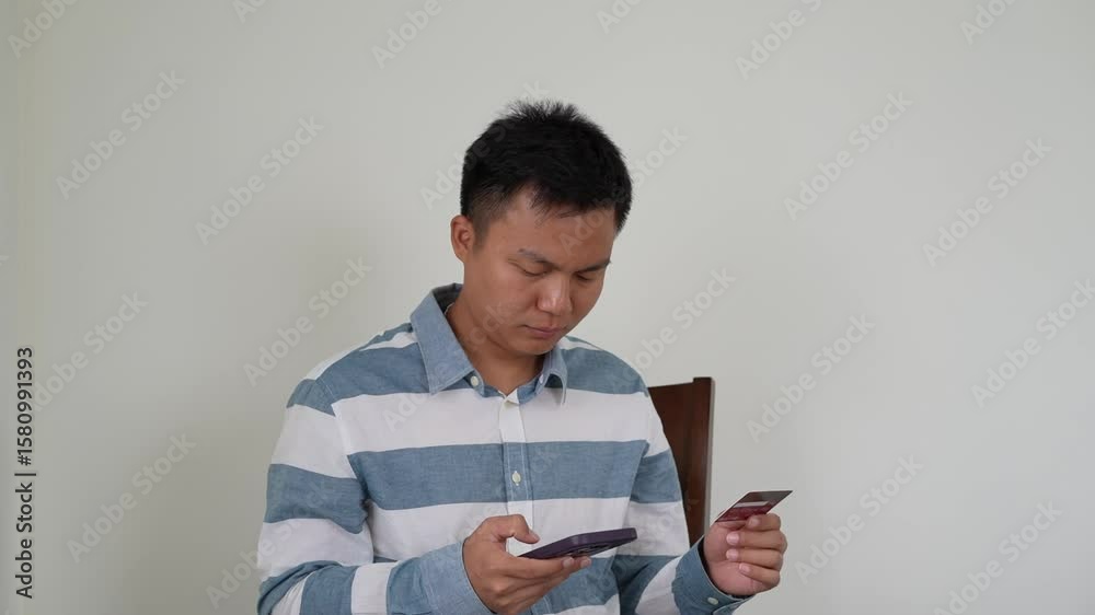 A young asian man is shopping online and holding mobile phone credit bank card payment for online pay, enter secure number authorization buy, purchase shopping internet banking, E-banking app service.