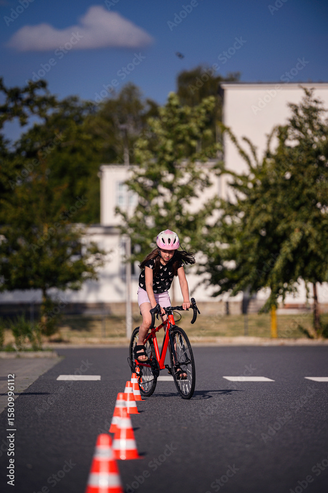 Obraz premium Young Girl Riding Bike Through Traffic Cones on Sunny Day