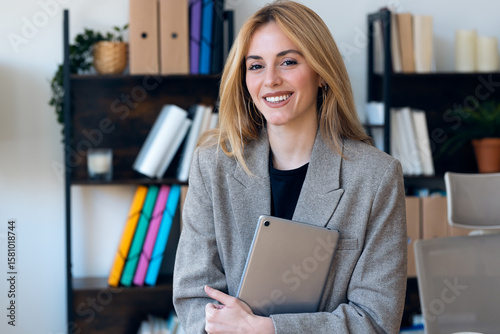 Beautiful lawyer woman working with digital tablet while looking at camera in her modern office