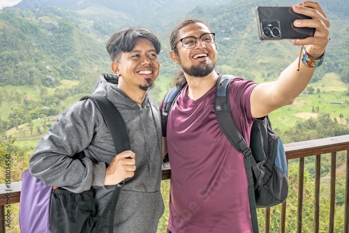 Two Latino men taking a selfie amidst a mountainous landscape. Two young happy men friends hikers taking a selfie in the mountain