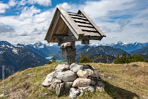 Rustic wooden summit cross overlooking majestic alpine peaks and a turquoise lake, ideal for hiking, outdoor, mountain and nature exploration in the european alps