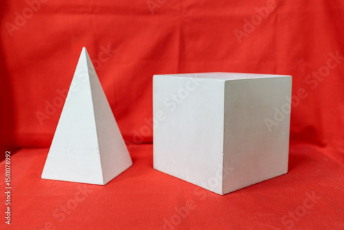 Two white shapes, one of which is a pyramid, are placed on a red background