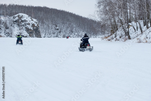 Two people are riding snowmobiles on a snowy road