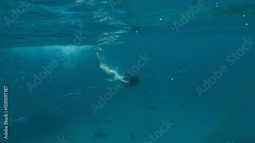 Young person in the blue sea surrounded by fishes