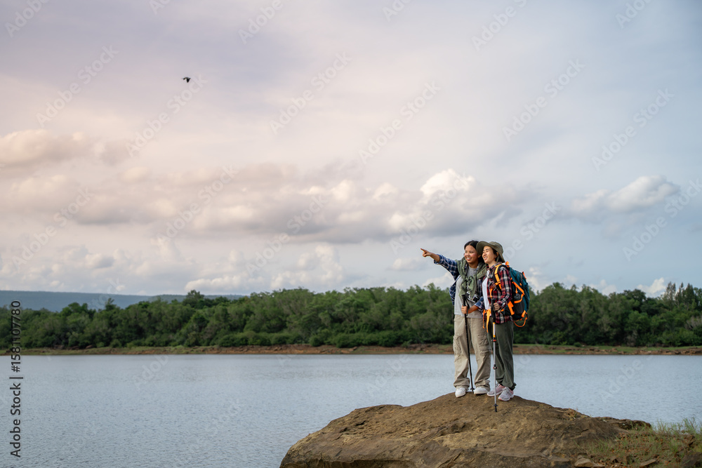 Obraz premium Two people standing on a rock overlooking a body of water. One of them is pointing at a bird flying in the sky