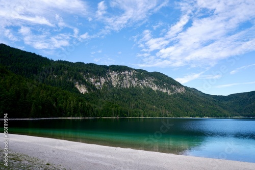 Kristallklarer Eibsee in Bayern mit Sandstrand und bewaldeten Bergen unter blauem Himmel