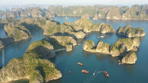 Limestone karst islands of Ha Long Bay rising from tranquil turquoise waters, featuring tourist boats gliding across scenic Vietnamese seascape under sunny summer sky