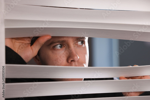 Bilde på lerret Paranoia. Worried man looking through window blinds indoors