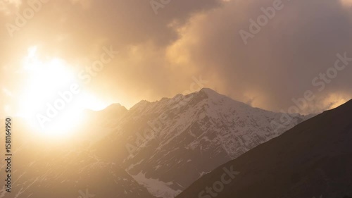 4K Zoom In Time-lapse shot of sunrays in front of snowy Himalayan mountain peak covered by clouds during the sunset at Lahaul Valley in Himachal Pradesh, India. Sun beam during the sunset in Himalayas